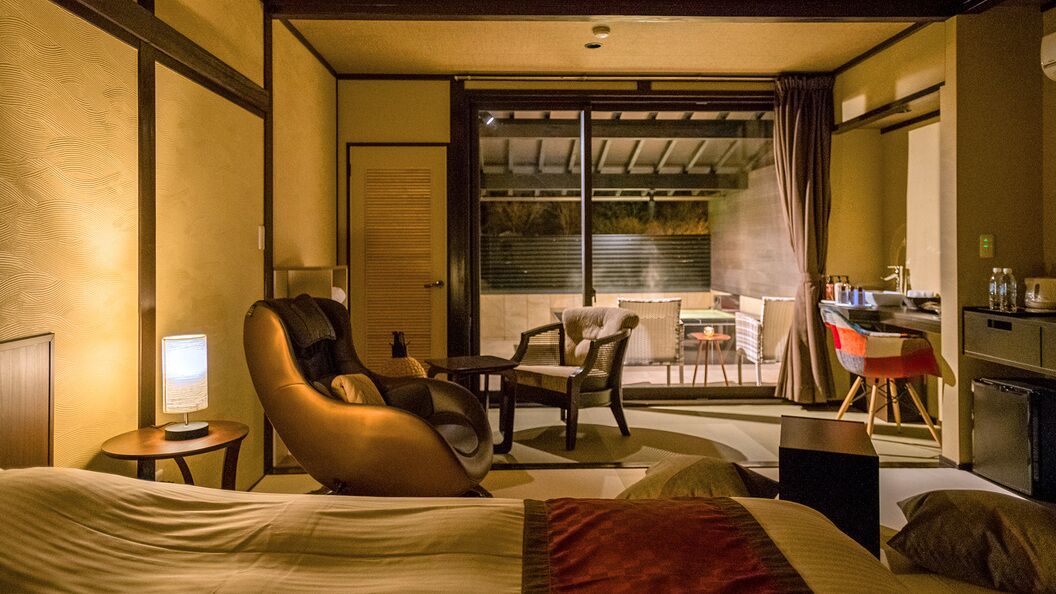 Ein Hotelzimmer mit Bett, Massagesessel, Schreibtisch und Balkon mit Tisch und Stühlen.