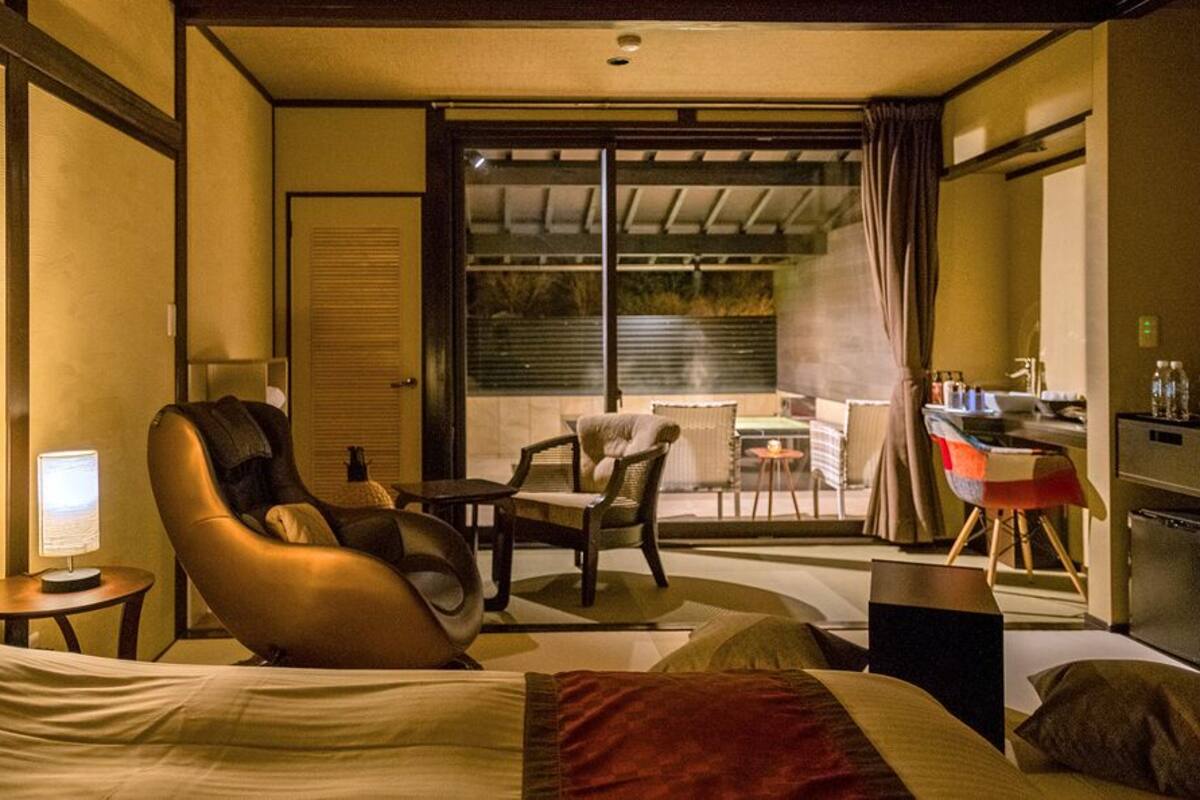 Une chambre d’hôtel équipée d’un lit, d’un fauteuil massant, d’un bureau et d’un balcon avec une table et des chaises.