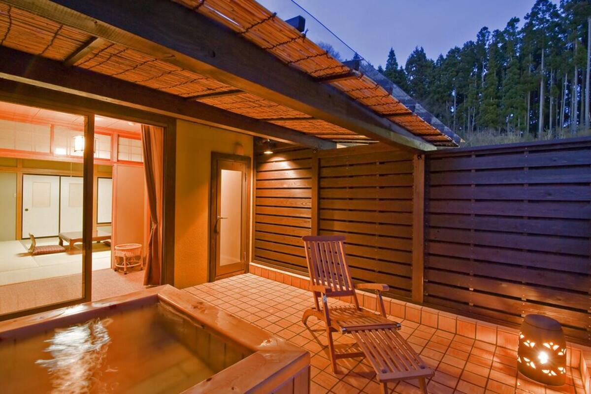 Une terrasse en bois avec un jacuzzi, une chaise et une lanterne.