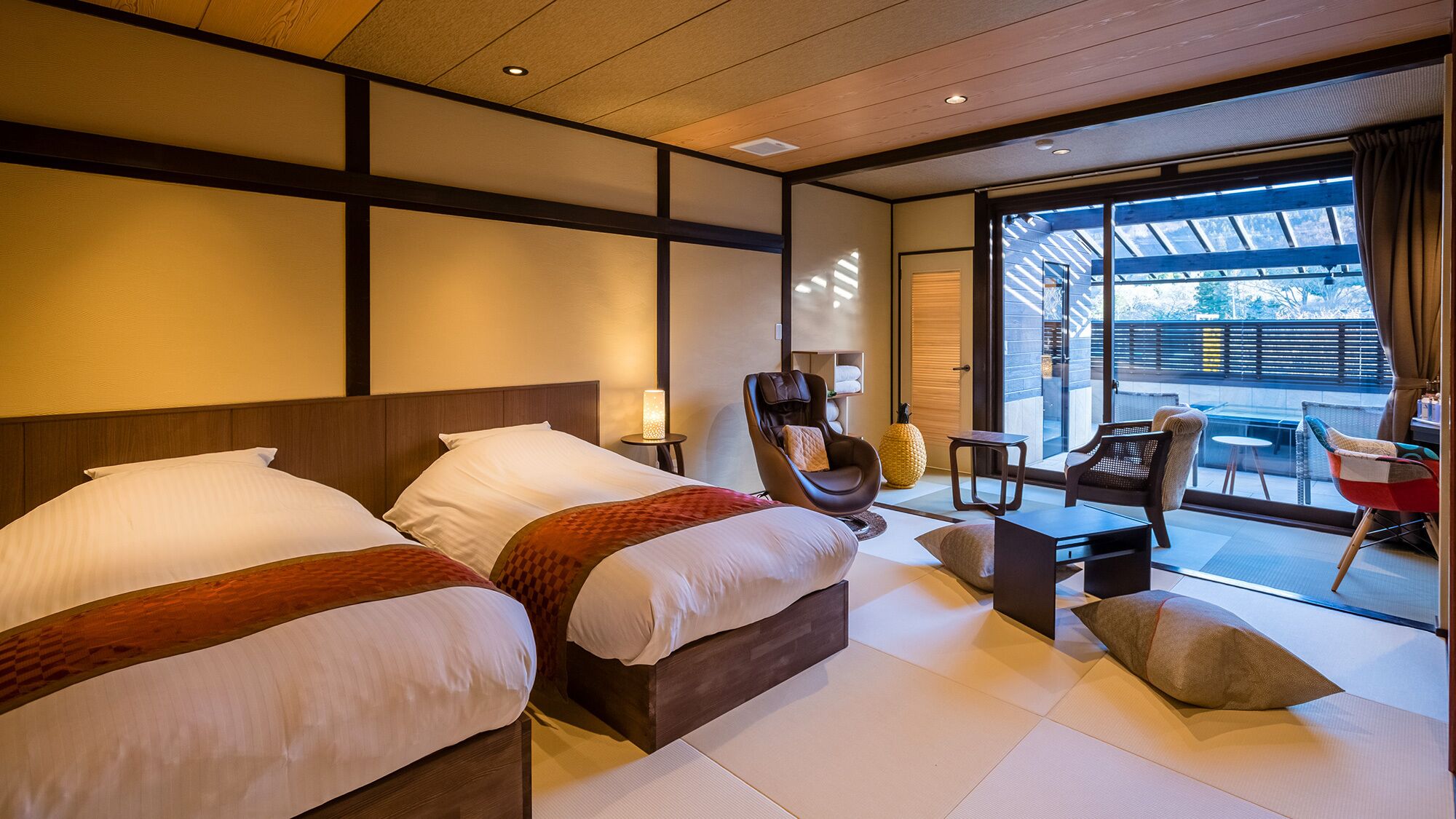 Ein Hotelzimmer mit zwei Betten, einem Massagesessel, einem kleinen Tisch und einem Balkon mit Sitzgelegenheit.