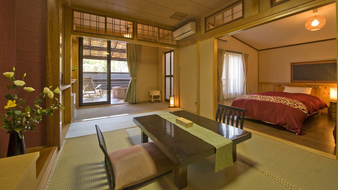 Ein traditioneller japanischer Raum mit Tatami-Boden, einem niedrigen Tisch, einem Bett mit roter Tagesdecke und einer Schiebetür, die zu einem Außenbereich führt.