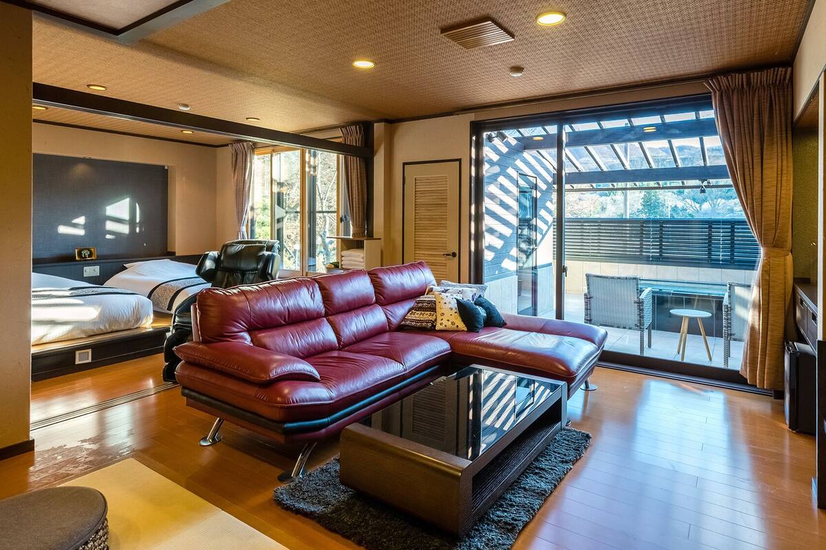 Une chambre d’hôtel moderne dotée d’un grand lit, d’un canapé en cuir, d’un fauteuil massant et d’un balcon avec vue.