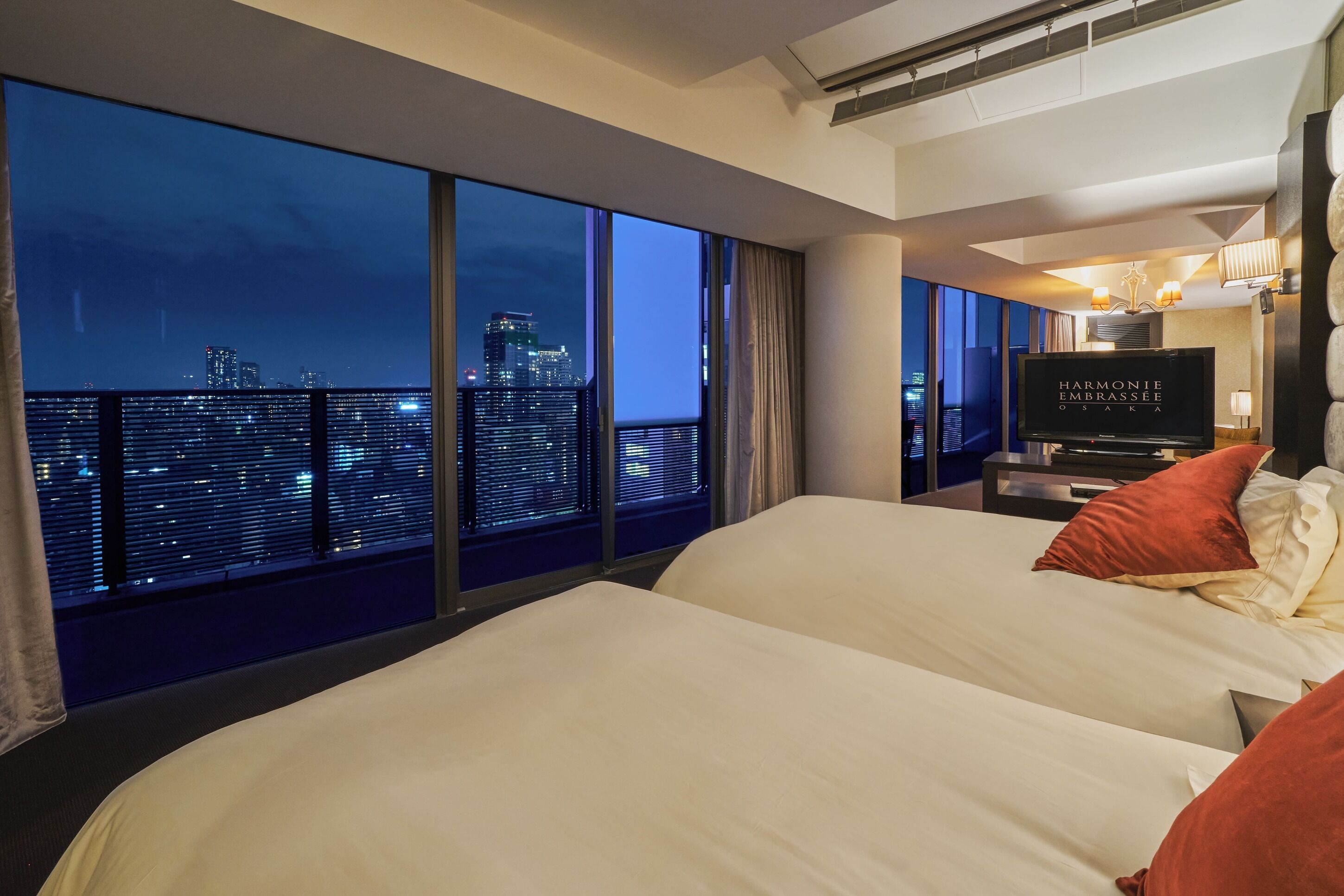 A hotel room with a large window, a bed, a television, and a city view.