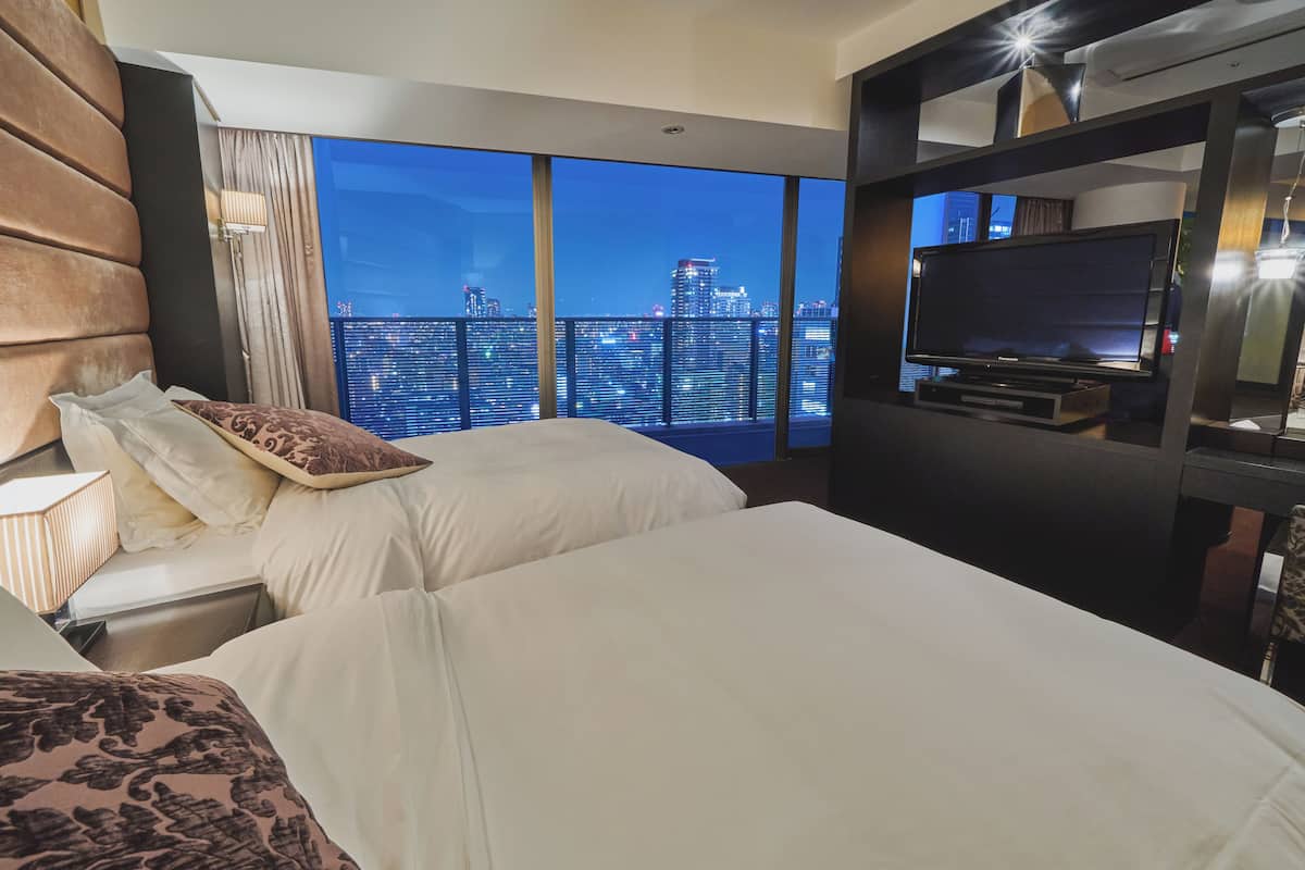 A hotel room with two beds, a TV, and a city view.
