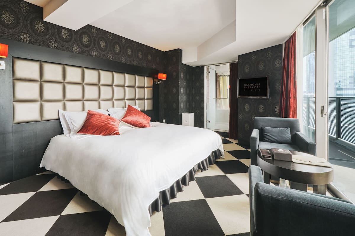 A modern hotel room with a large bed, a sofa, a small table, and a view of the city.