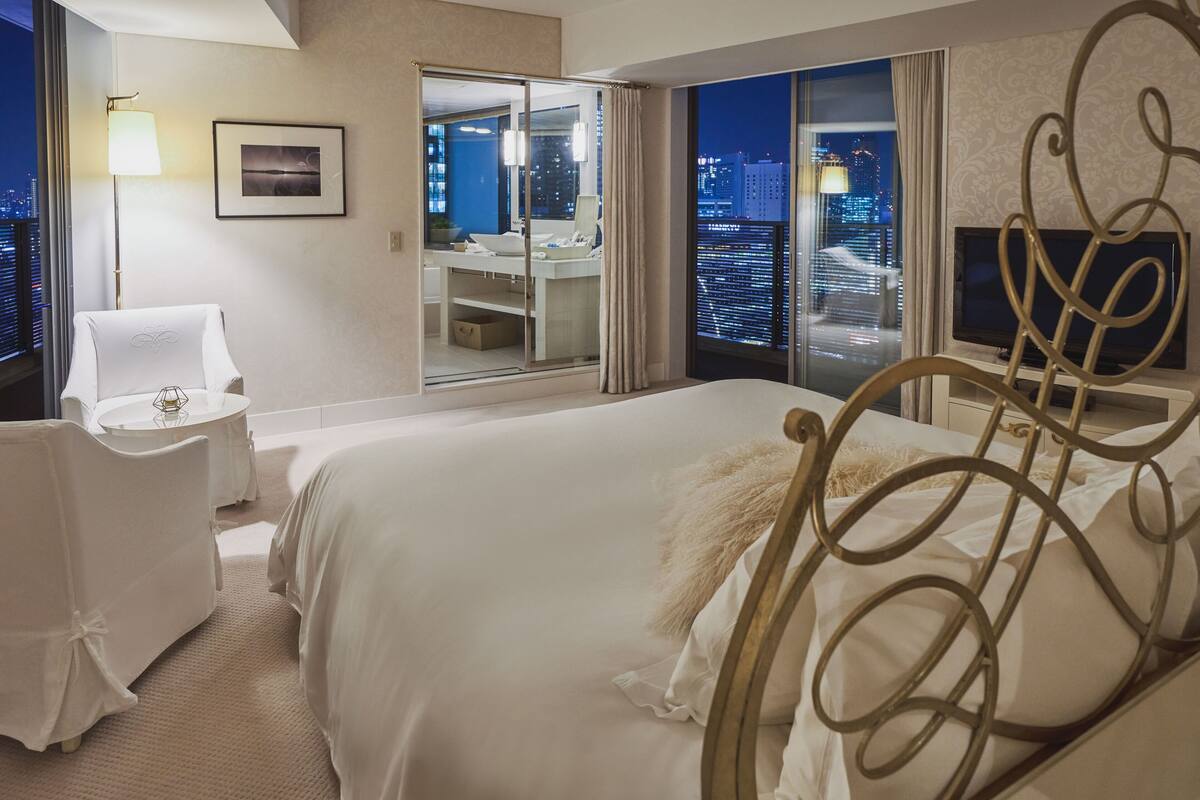 A hotel room with a bed, a desk, a chair, a TV, and a bathroom with a city view.