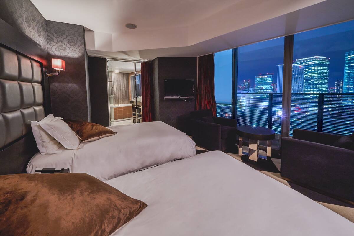A hotel room with two beds, a TV, a small table, and a city view.