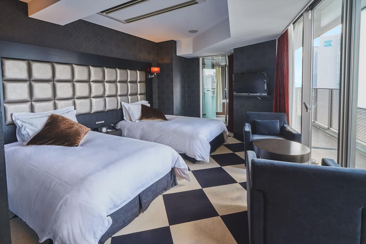 A hotel room with two beds, a TV, a small table, and a view of the city.