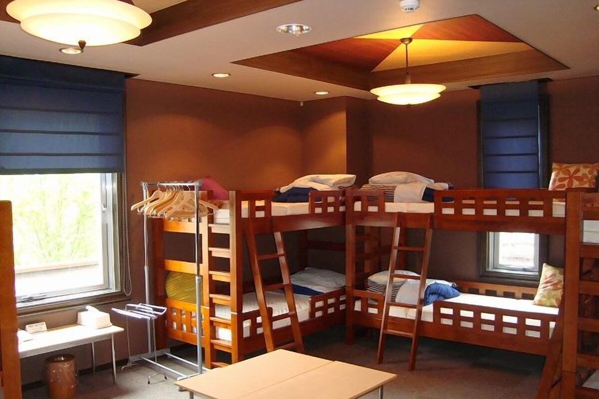 Een slaapkamer met een stapelbed, een tafel en een raam.