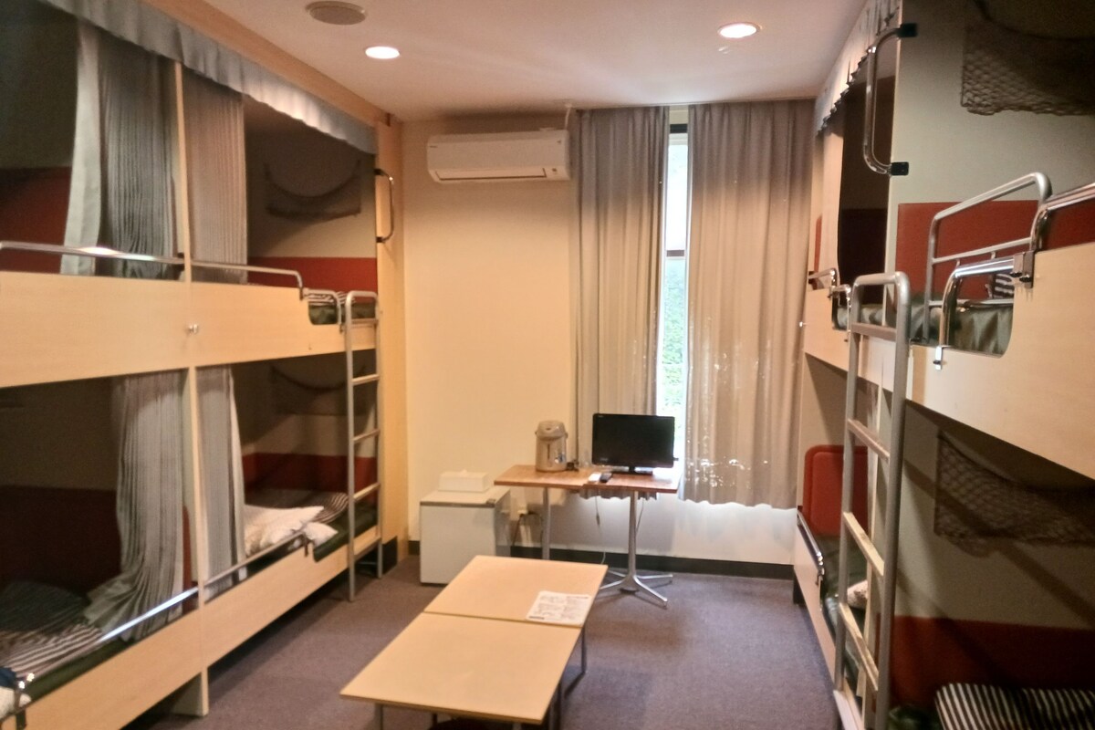 Een slaapkamer met stapelbedden, een bureau met computer en een raam met gordijnen.