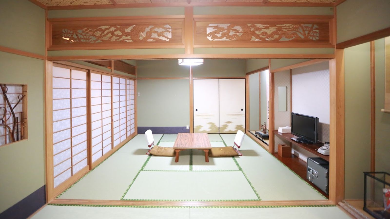 Um quarto japonês tradicional com tatames, uma mesa baixa, almofadas, portas corrediças e uma televisão.