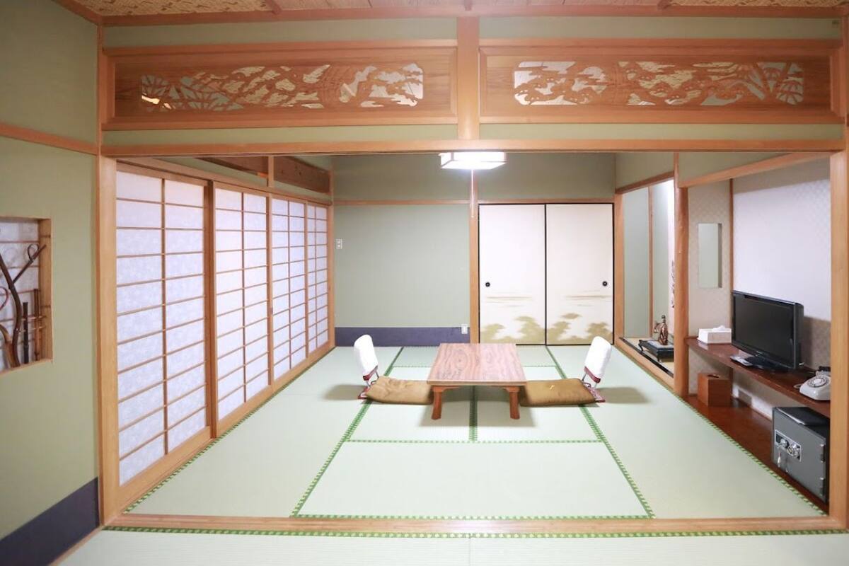 Una habitación japonesa tradicional con suelo de tatami, una mesa baja, cojines, puertas correderas y un televisor.