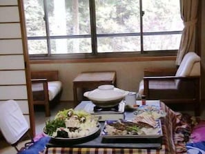 A dining area with a table set for a meal, a window with a view of trees, and a sofa. - Takao Kanko Hotel (Kyoto)