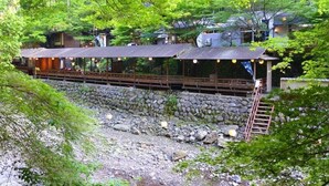 Een traditionele Japanse ryokan met houten constructie, een pad van stenen en weelderige begroeiing.