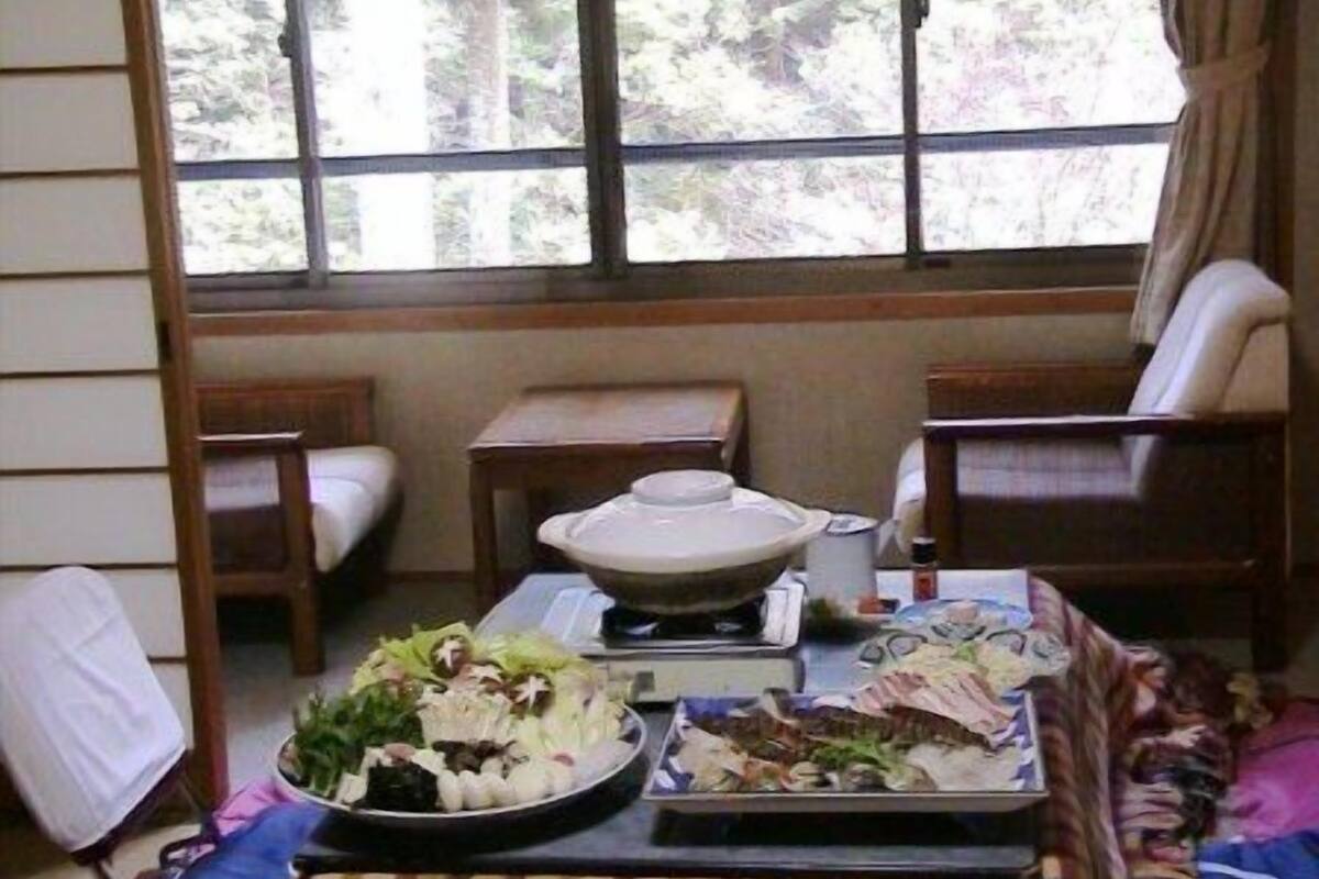 Un comedor con una mesa dispuesta para comer, una ventana con vistas a árboles y un sofá.