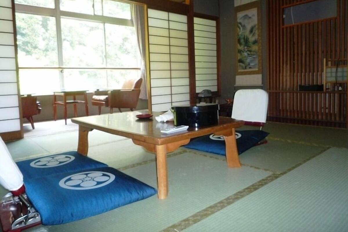 Una habitación con esteras de tatami, una mesa baja, cojines y puertas correderas.