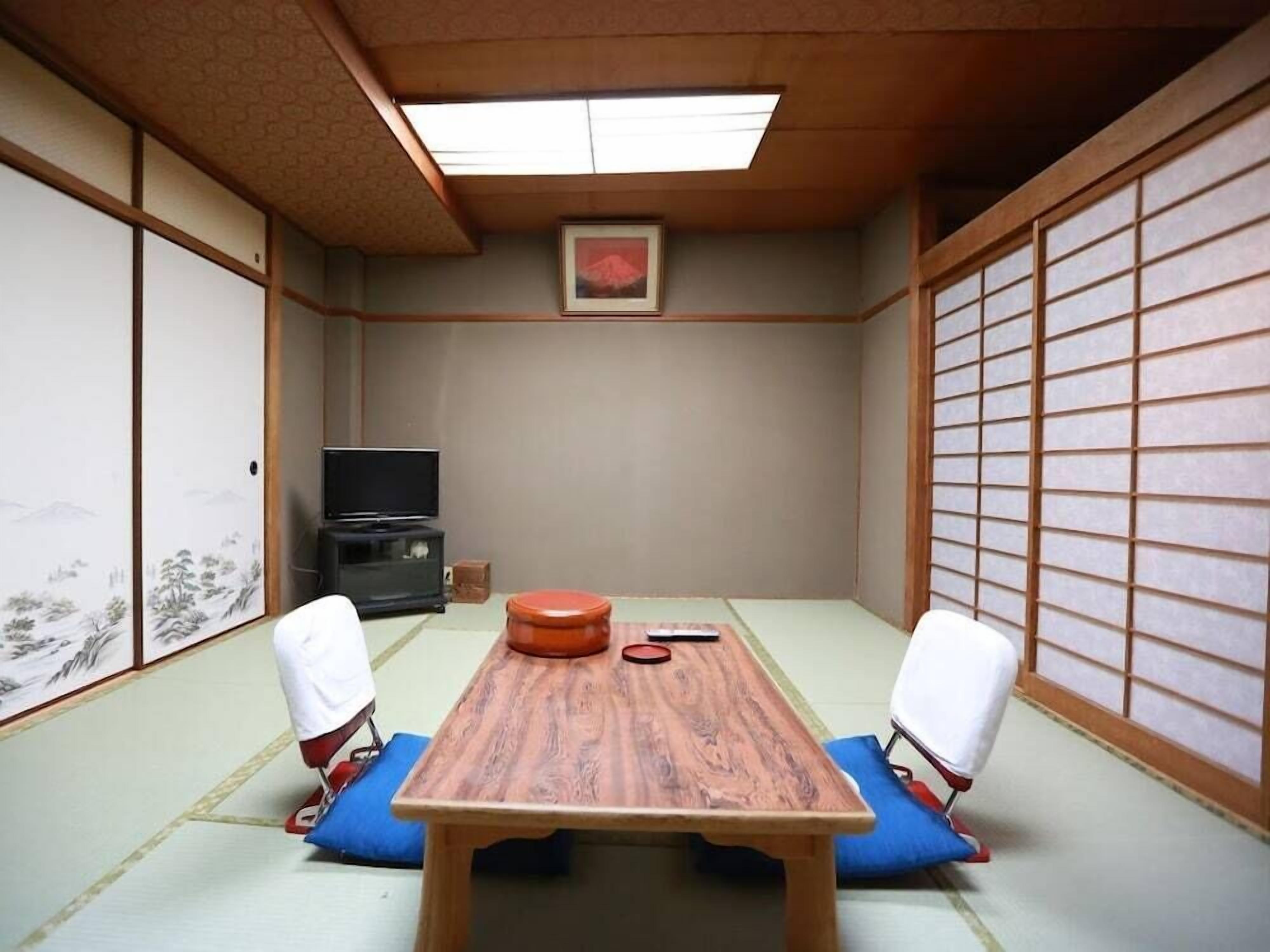 A traditional Japanese room with tatami flooring, a low table, two chairs, a television, and a sliding door.