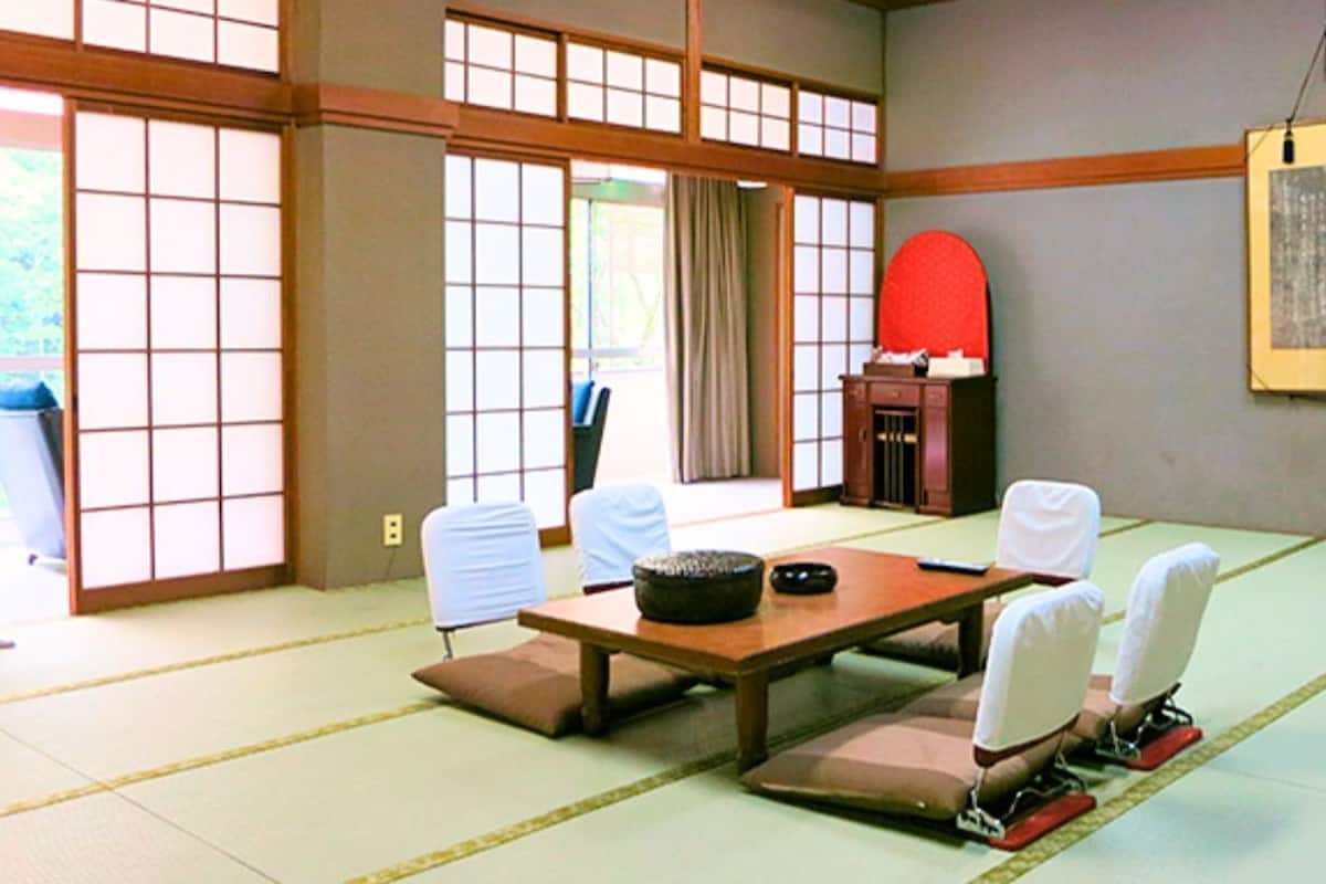 Una habitación con esteras tatami, una mesa baja y sillas, un rincón rojo y un cuadro en la pared.
