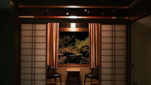 Een traditionele Japanse kamer met tatami vloerbedekking, een lage tafel, twee stoelen en uitzicht op een koimeer door shoji schermen.