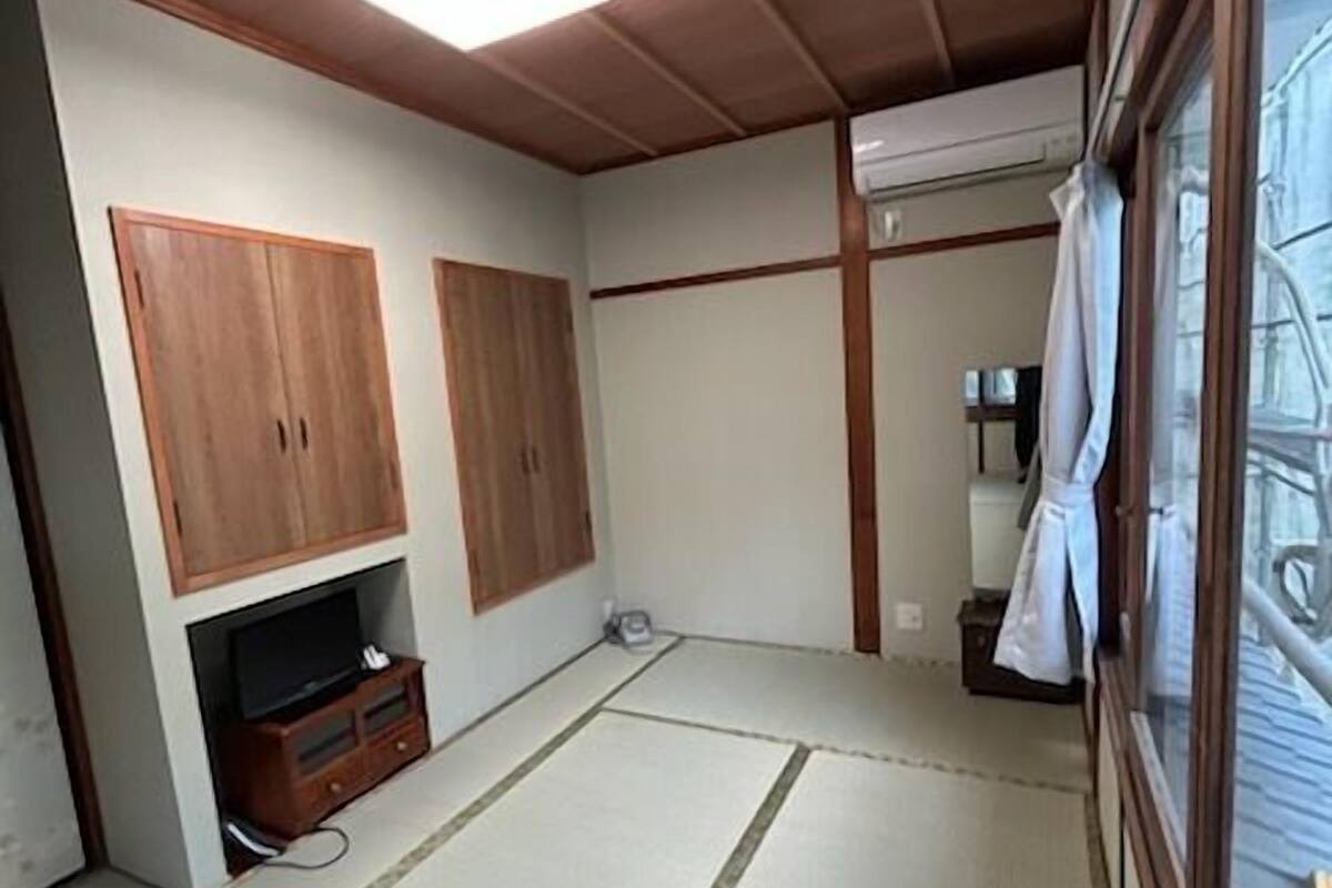 Una habitación con suelo de tatami, armarios de madera, televisor y ventana con cortina.