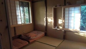Ein traditioneller japanischer Raum mit Tatami-Boden, einem niedrigen Bett mit Kissen und verschiebbaren Shoji-Türen.