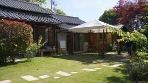 Ein traditionelles japanisches Haus mit Ziegeldach, einem kleinen Garten mit Trittsteinen und einer überdachten Sitzterrasse.