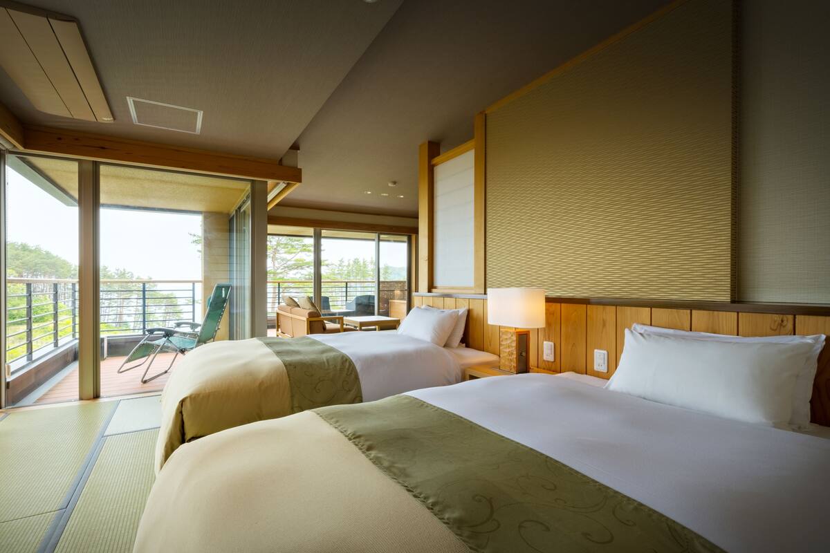 A hotel room with two beds, a balcony with a chair, and a large window.
