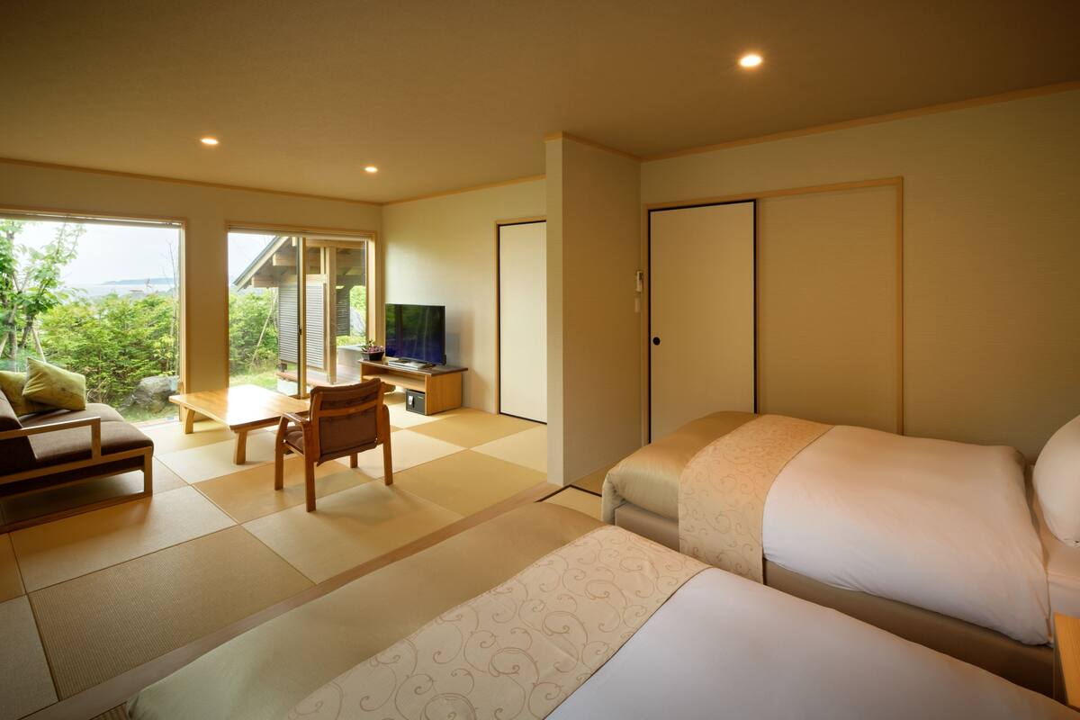 A hotel room with a bed, a sofa, a TV, and a sliding door leading to a balcony.