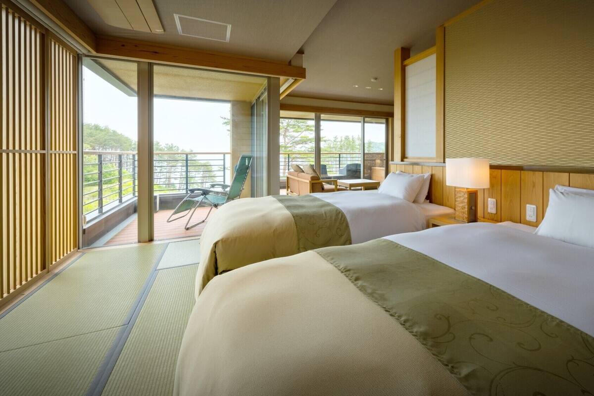 A hotel room with two beds, a balcony with a view, and a small table with chairs.