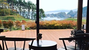 Una terraza con dos sillas y una mesa, con vistas a un paisaje costero con árboles y colinas.