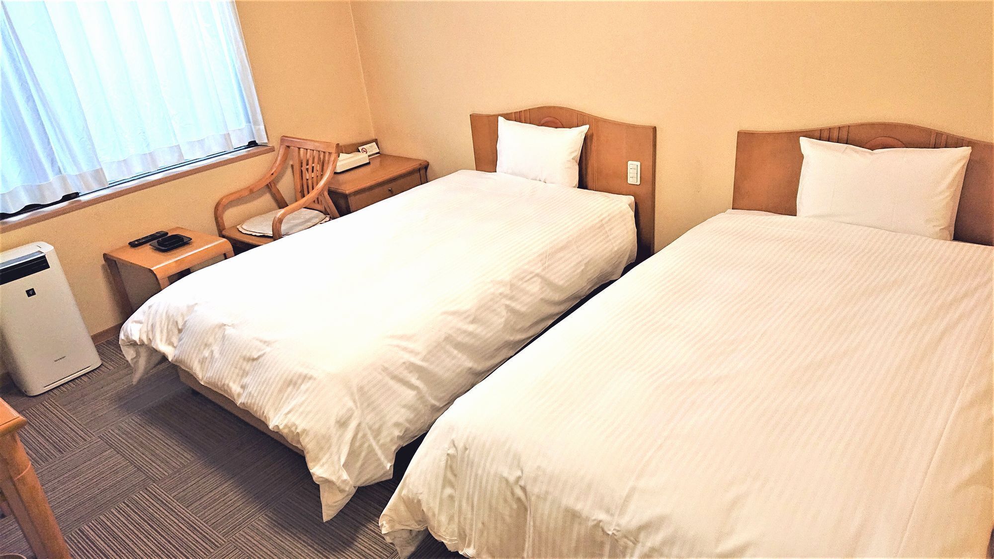 Habitació d'hotel amb dos llits individuals, una taula de treball amb cadira, una taula petita i una finestra amb cortines.