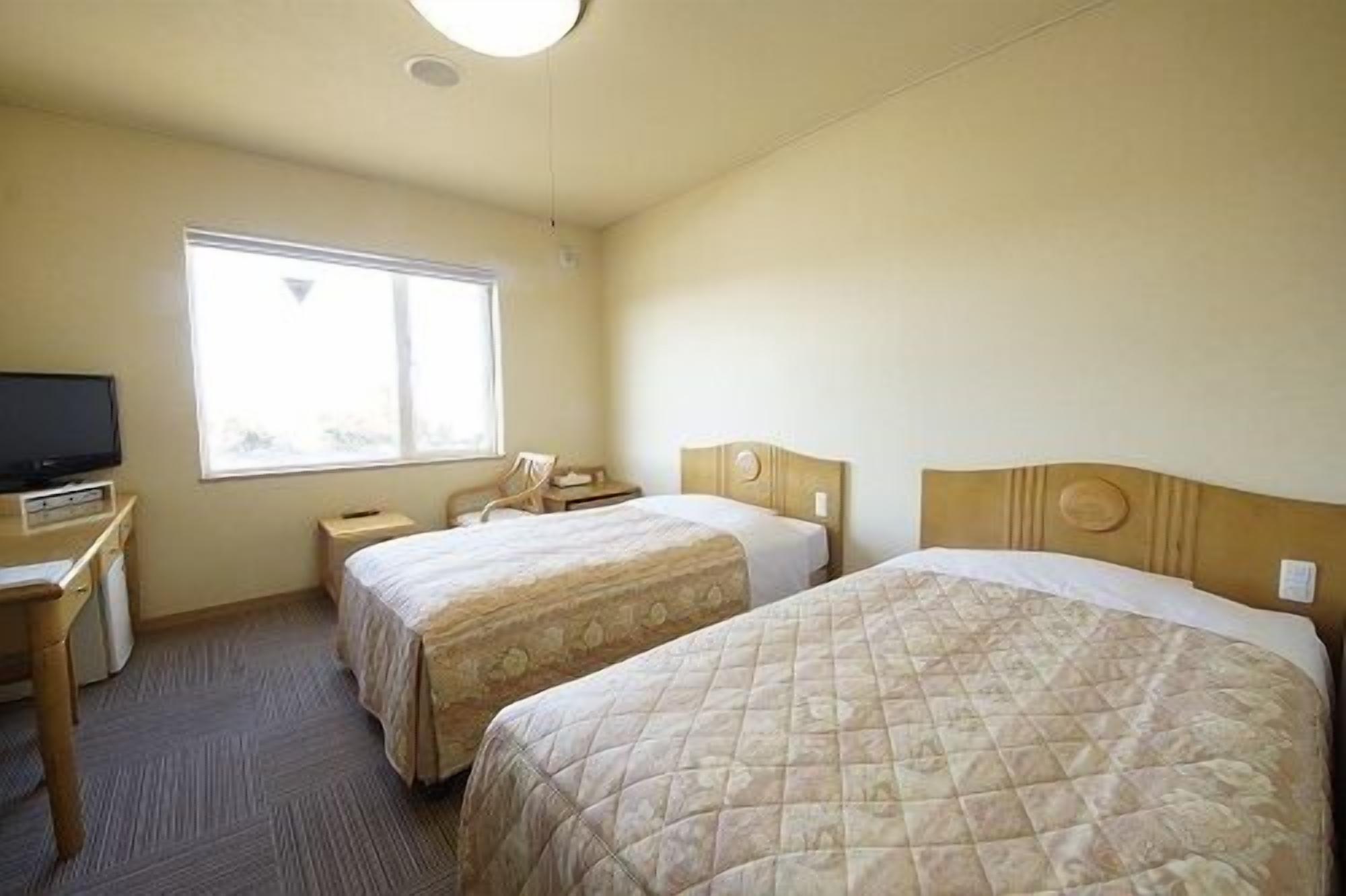 A hotel room with two beds, a television, a window, and a desk.