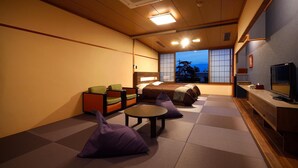 A room with tatami mat flooring, a low table, a sofa, and a bed with a view of the outside. - Isawa Onsenkyo Ryokan Kisen (Fuefuki)