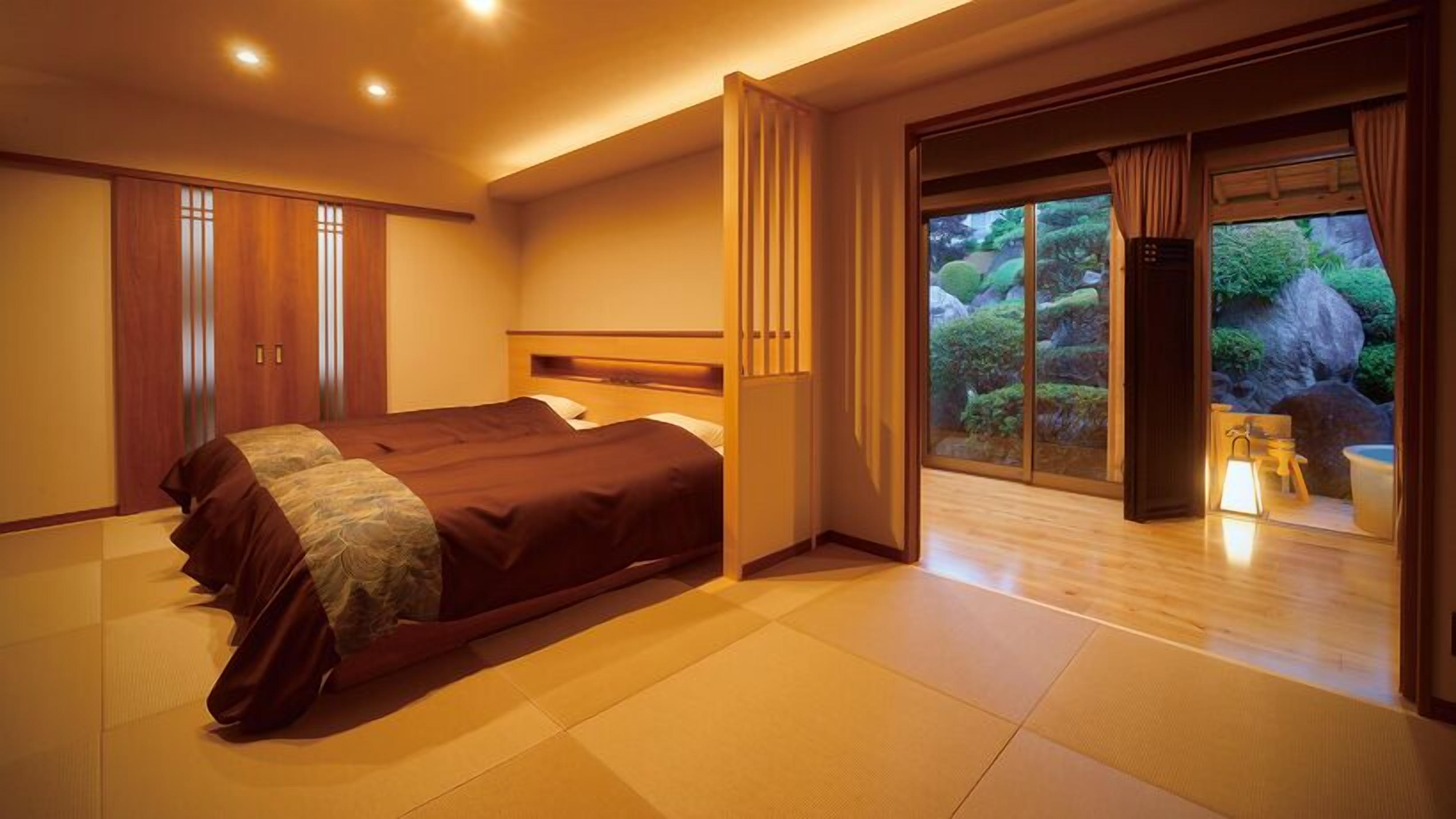 A hotel room with a large bed, sliding glass doors to a garden, and a wooden wardrobe.