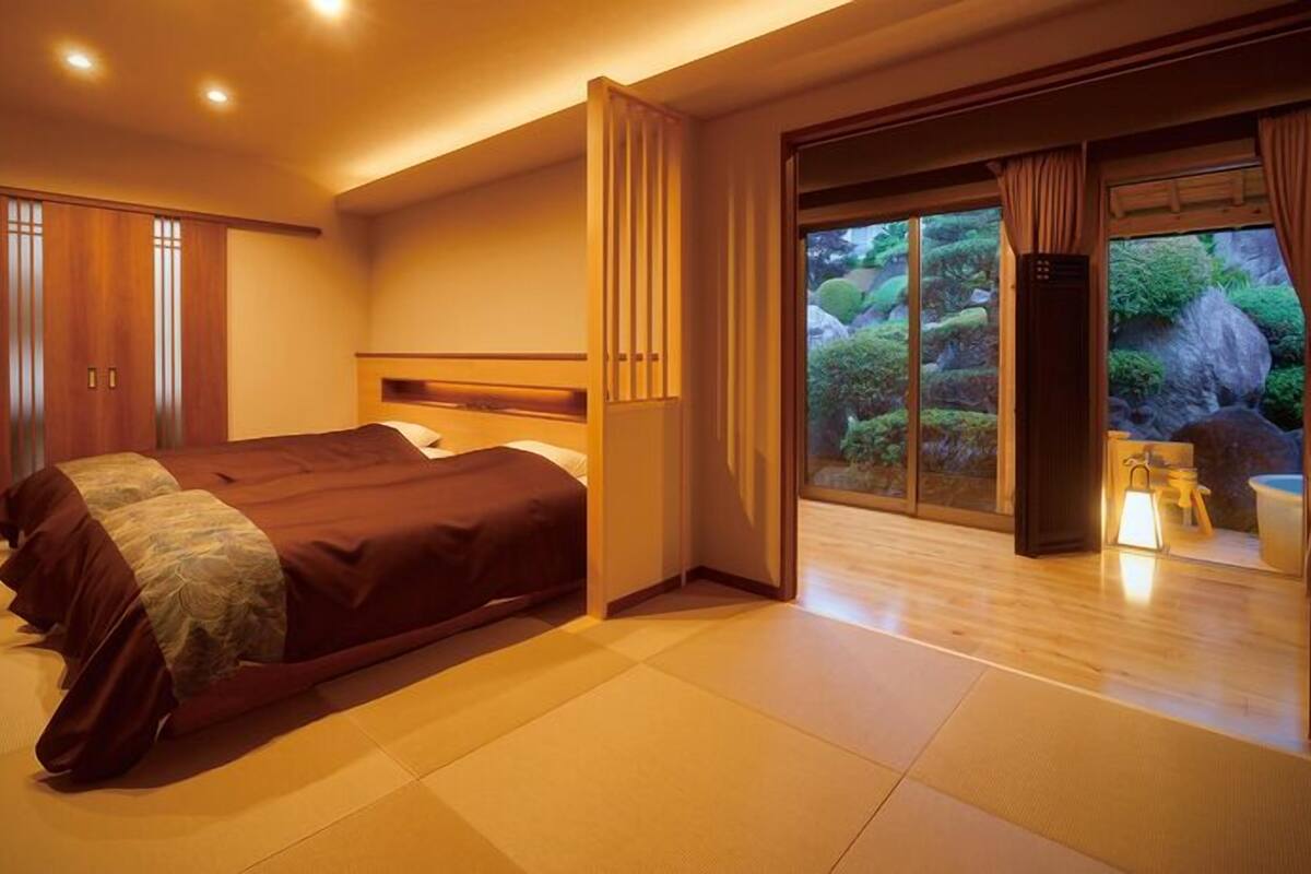 Une chambre d’hôtel avec un grand lit, des portes-fenêtres coulissantes donnant sur un jardin et une armoire en bois.