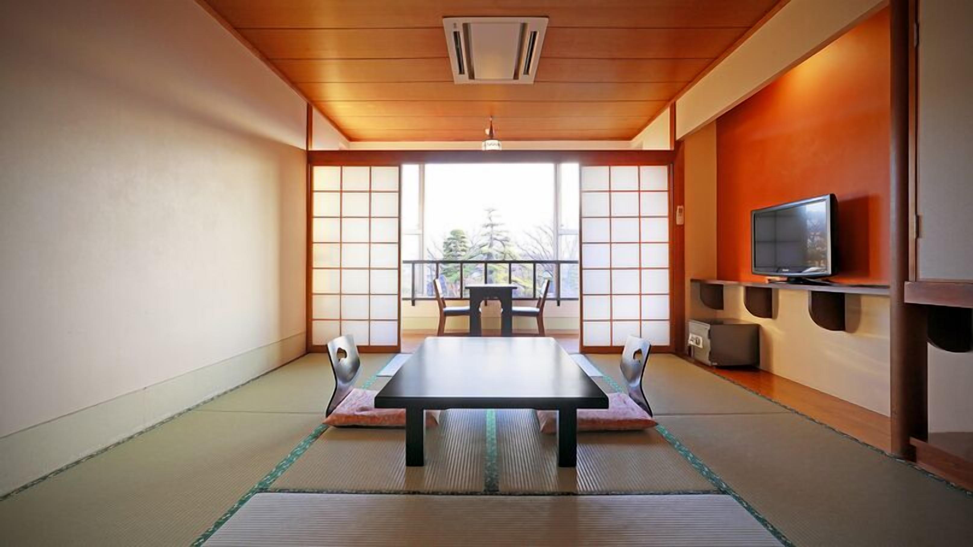 A traditional Japanese room with tatami flooring, a low table with cushions, sliding doors, and a television on a shelf.