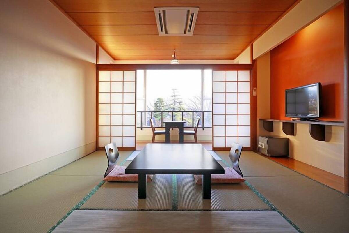 Une pièce de style japonais traditionnel, avec un sol recouvert de tatamis, une petite table basse entourée de coussins, des portes coulissantes et un téléviseur posé sur une étagère.