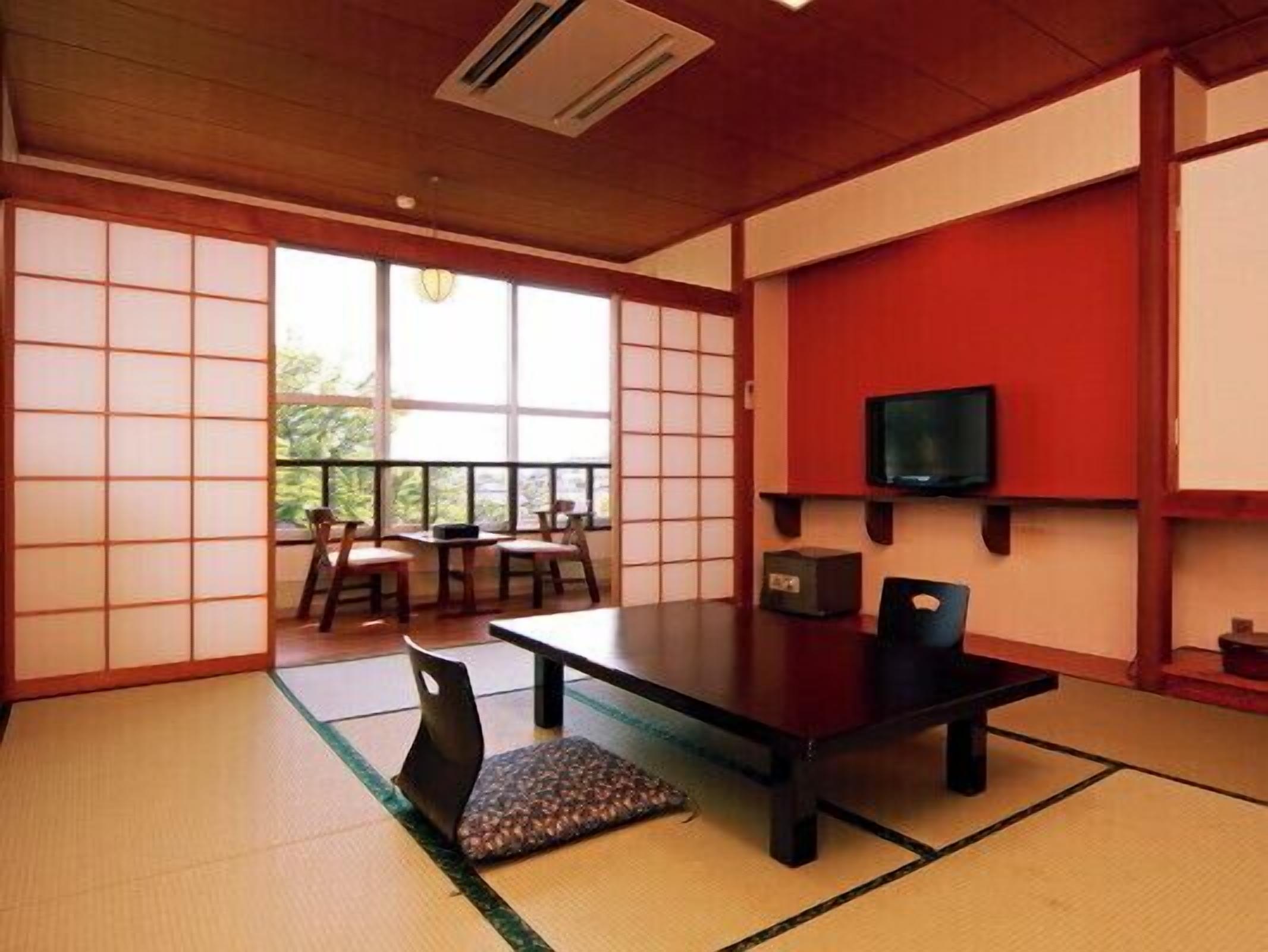 Une pièce de style japonais traditionnel, avec un sol recouvert de tatamis, une table basse, des chaises, un téléviseur et une porte coulissante donnant sur un balcon.