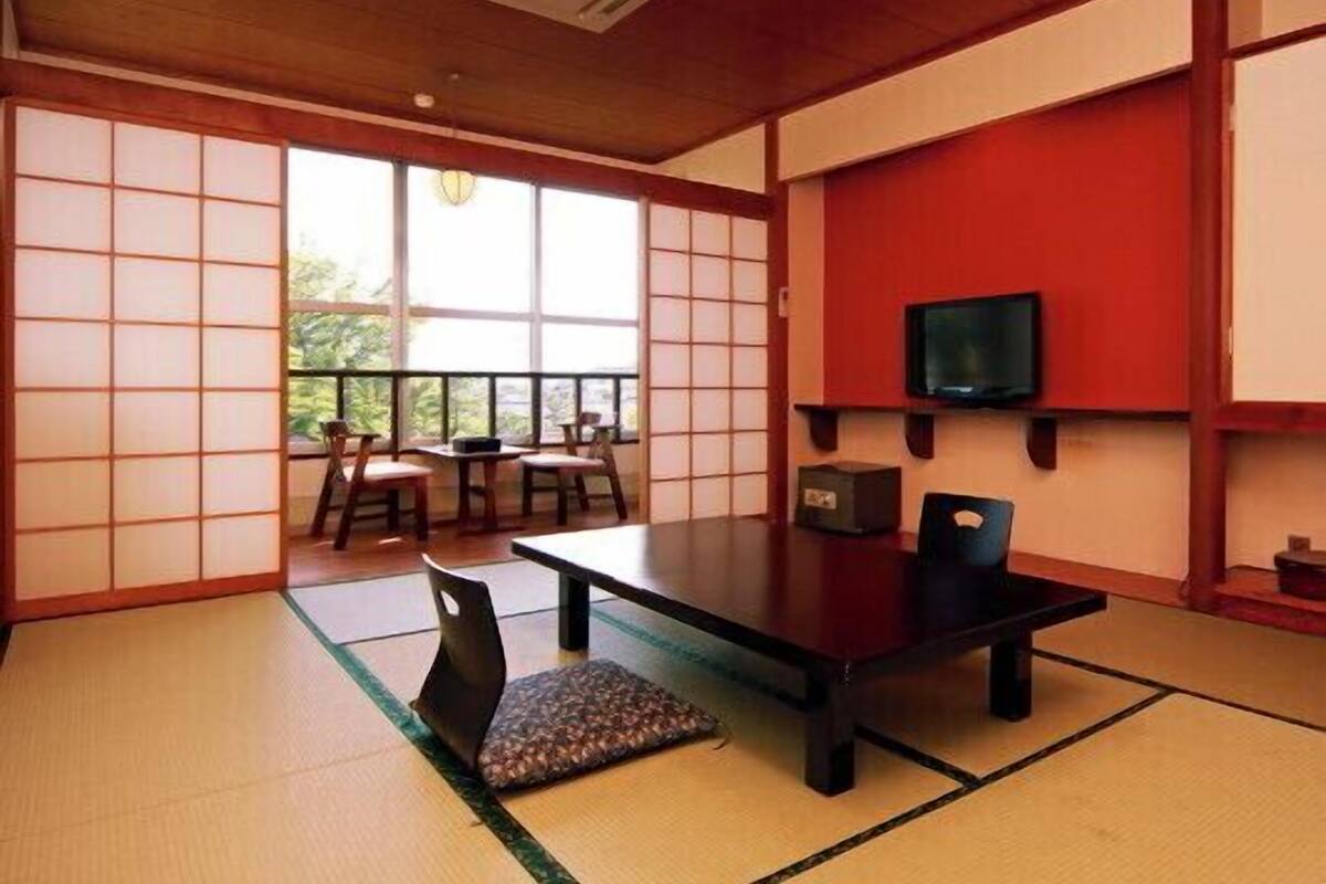 Une pièce de style japonais traditionnel, avec un sol recouvert de tatamis, une table basse, des chaises, un téléviseur et une porte coulissante donnant sur un balcon.
