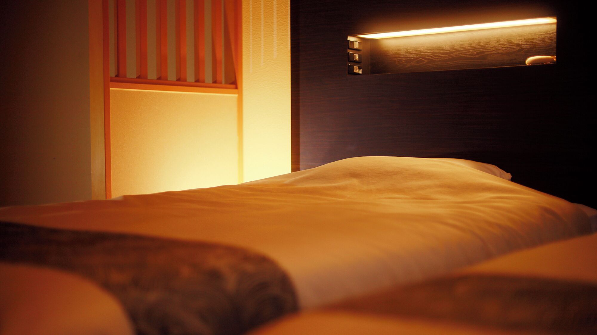 Une chambre d’hôtel avec un lit, une table de chevet et un luminaire fixé au mur.