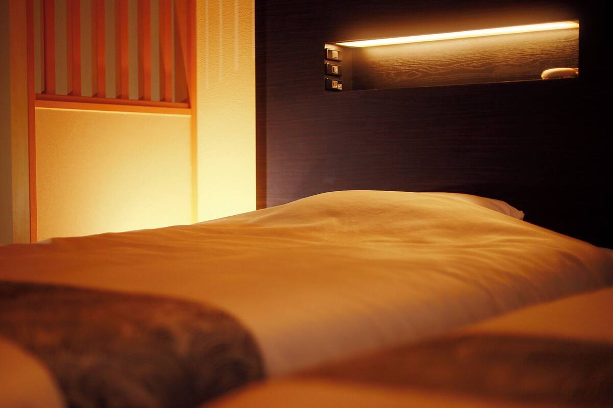 Une chambre d’hôtel avec un lit, une table de chevet et un luminaire fixé au mur.