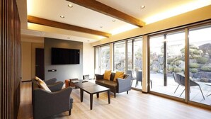 A modern living room with a TV, sofas, a coffee table, and large sliding glass doors to an outdoor garden. - Isawa Onsenkyo Ryokan Kisen (Fuefuki)