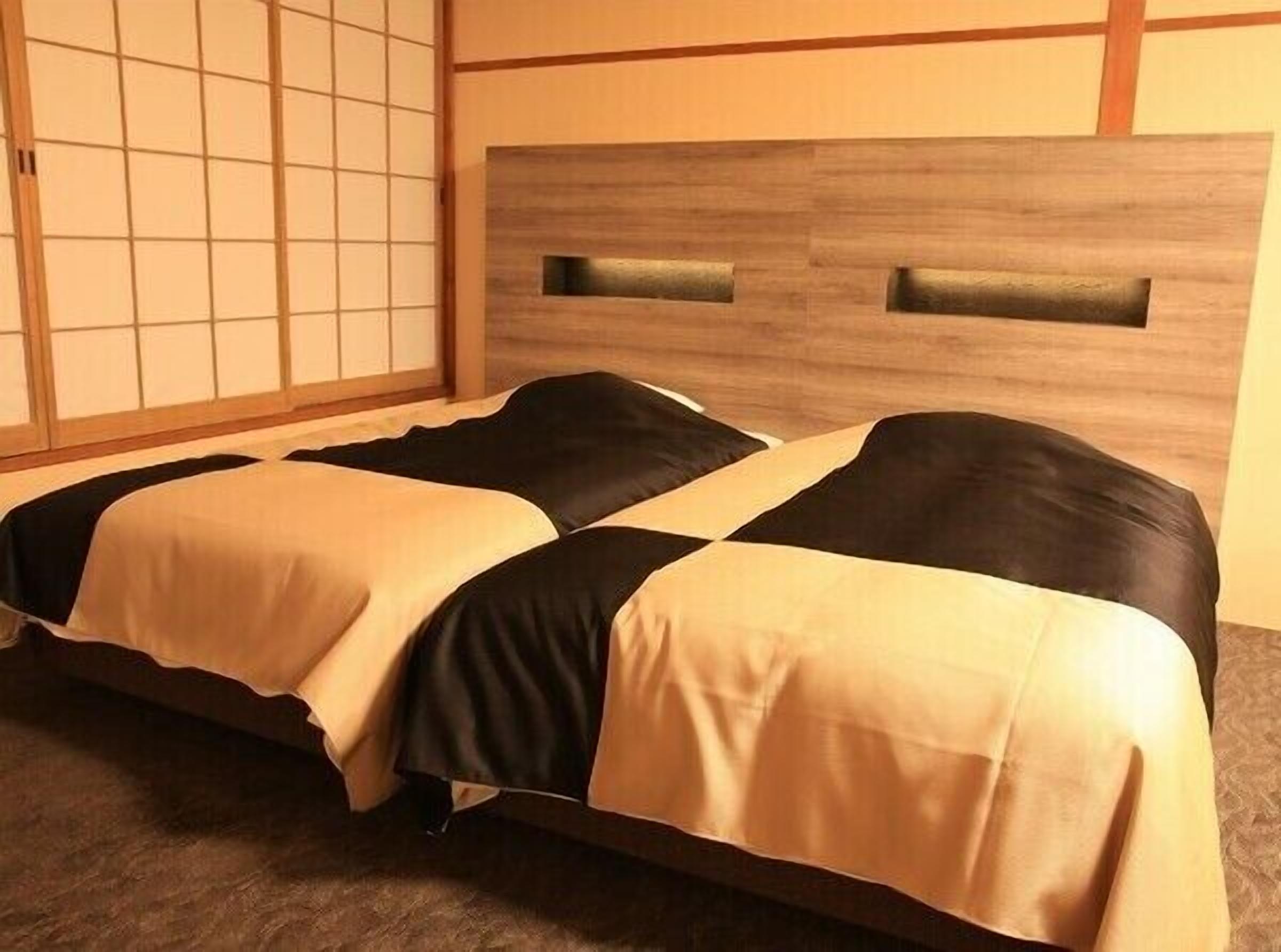 Une pièce avec un lit, une tête de lit en bois et un paravent japonais.