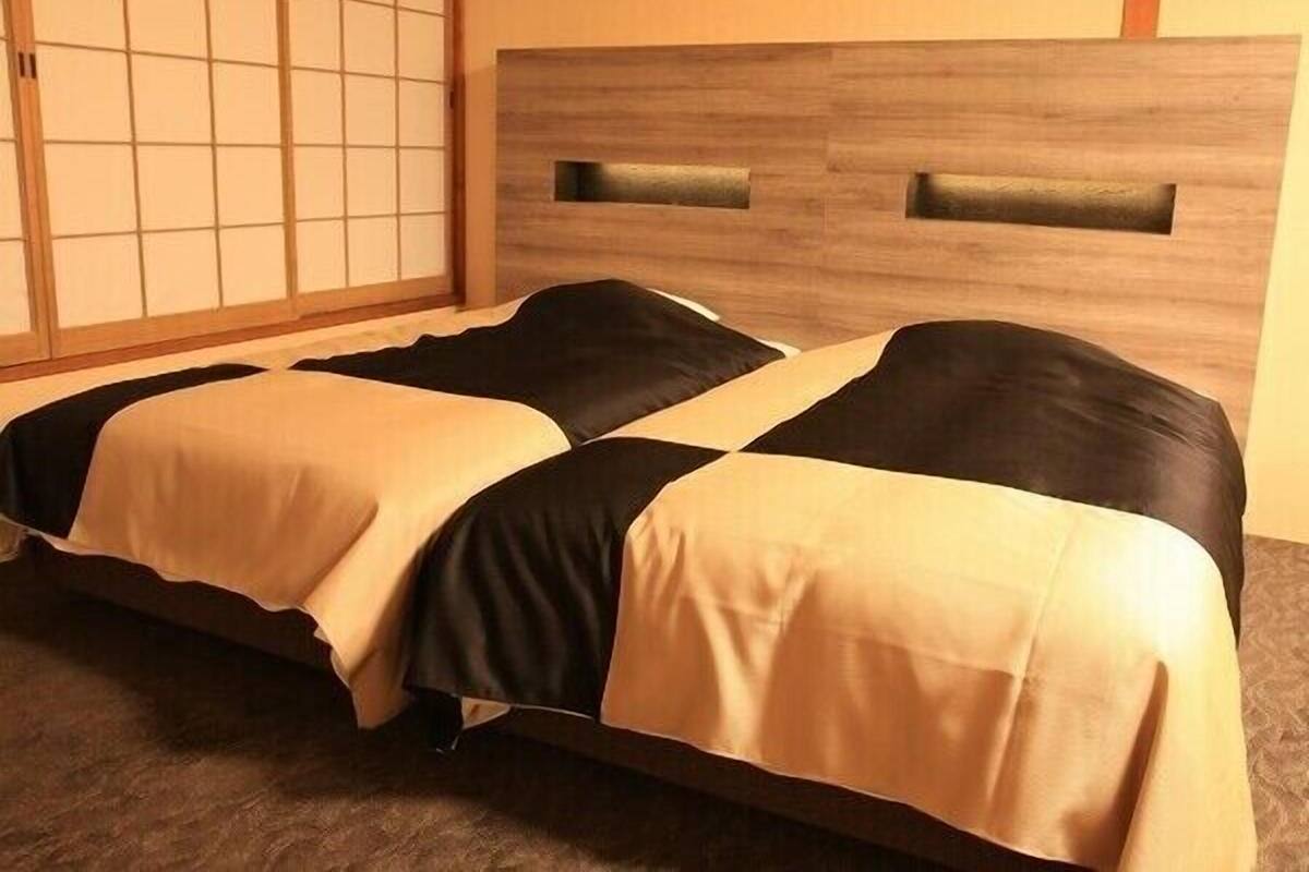 Une pièce avec un lit, une tête de lit en bois et un paravent japonais.