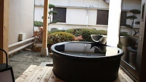 A hot tub on a wooden deck with a view of a building and a garden. - Isawa Onsenkyo Ryokan Kisen (Fuefuki)