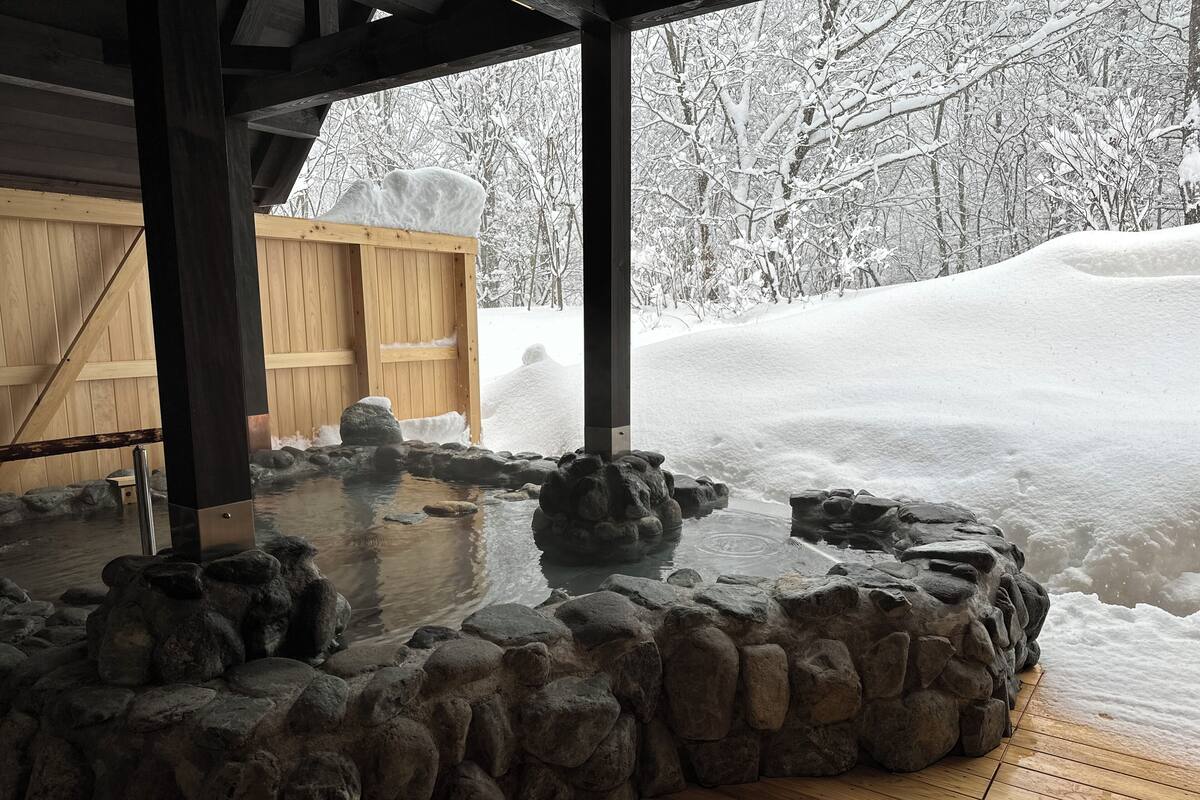 A stone hot tub area with a wooden deck, surrounded by snow-covered landscape.