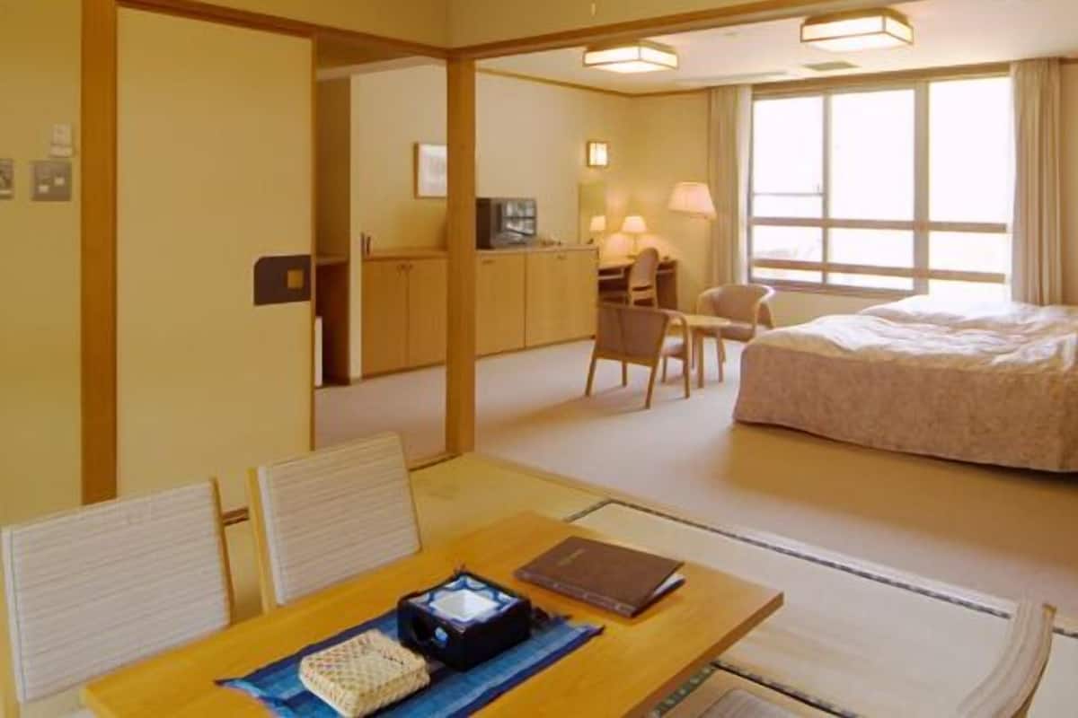 A hotel room with a bed, a desk, a chair, and a dining table.