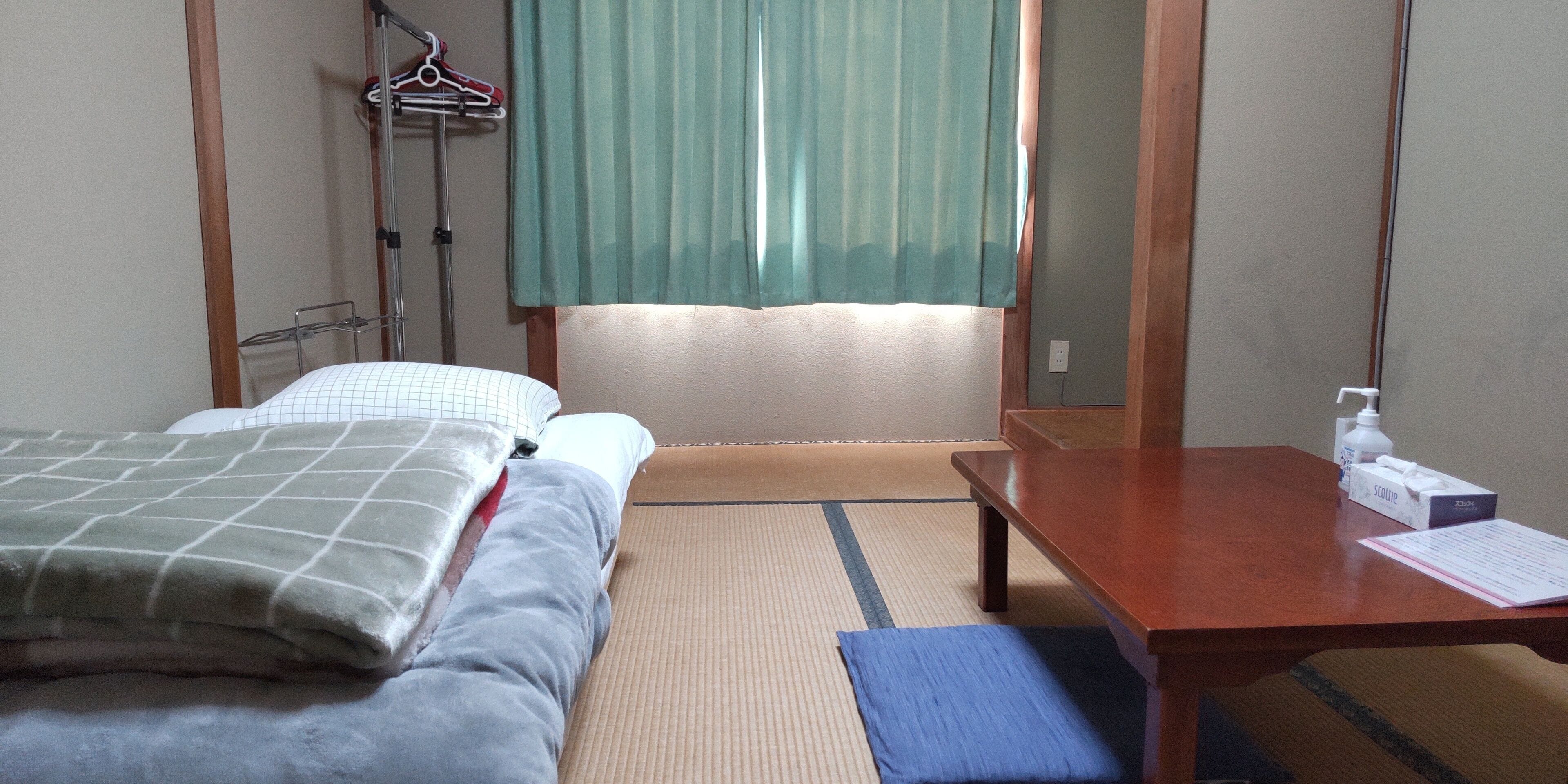Een hotelkamer met een bed, een houten tafel, een stoel, een spiegel en een raam met gordijnen.