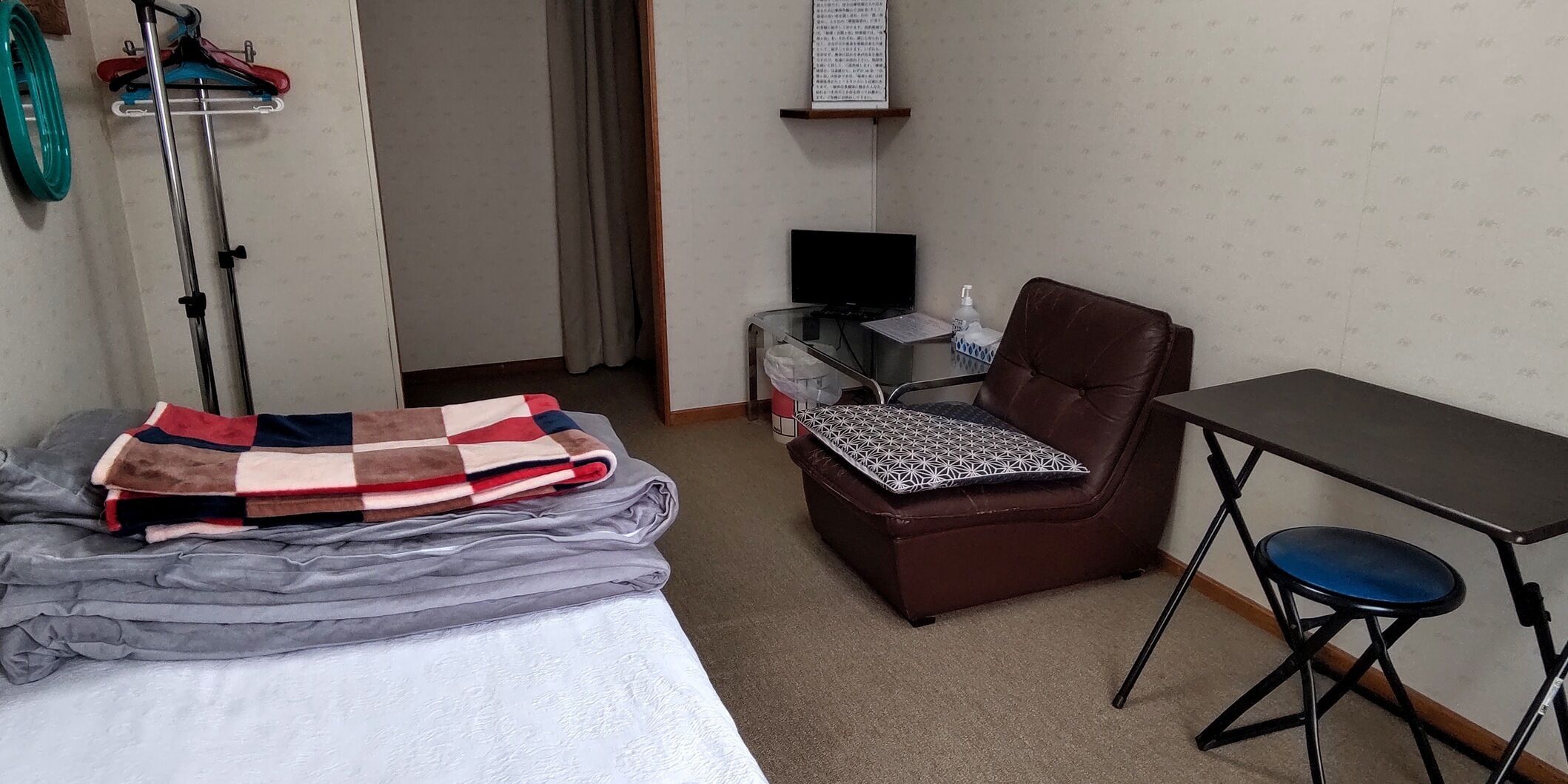 Hotelkamer met een bed, een stoel, een tafeltje, een televisie en een wandplank.