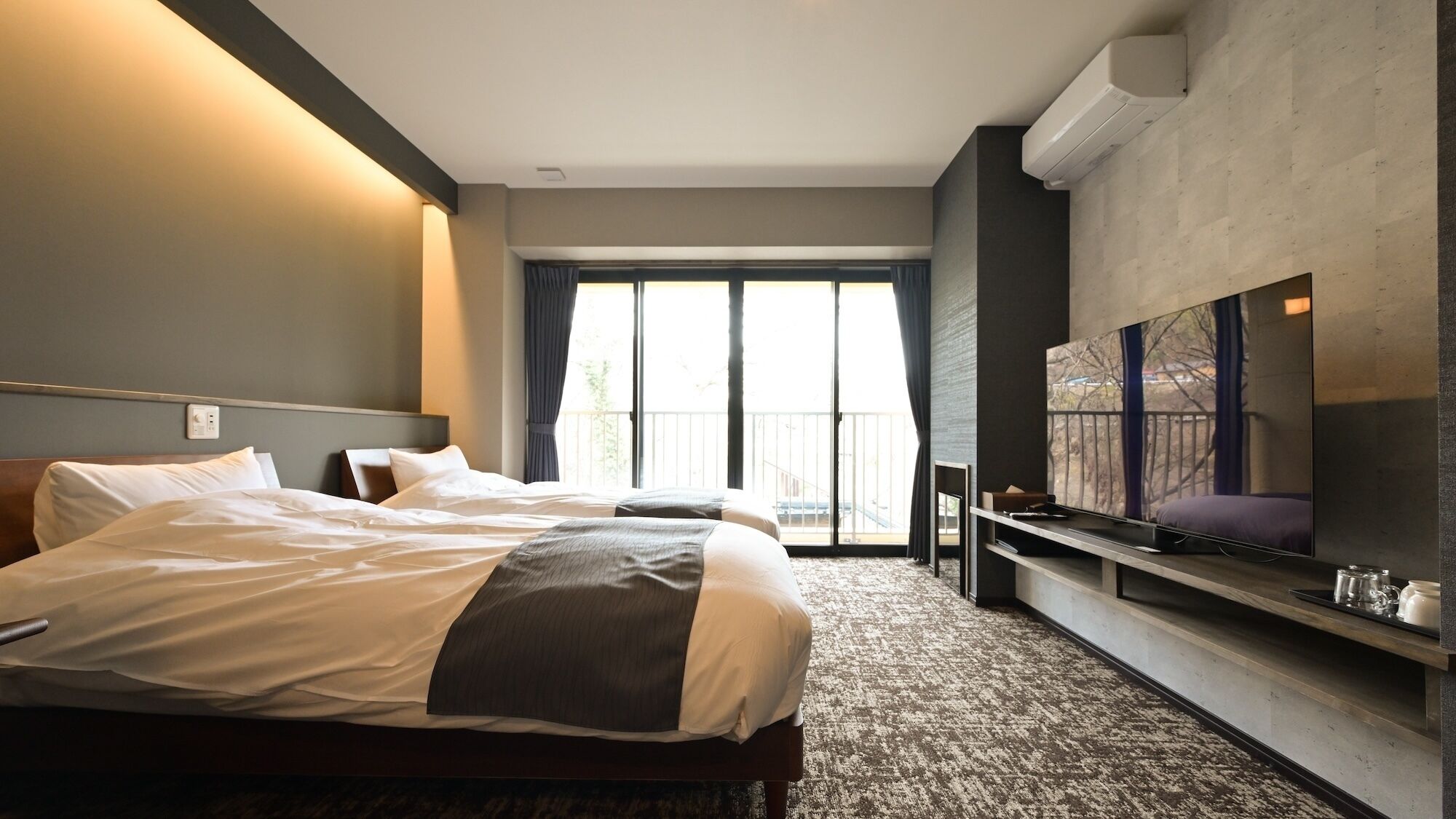 Ein Hotelzimmer mit einem großen Bett, einem flachbildfernseher an der Wand und einem Balkon mit Blick.